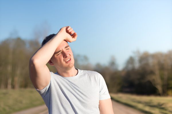 joven atleta recibió el sol y el golpe de calor y dolor de cabeza. chico sostiene la cabeza con las manos y se protege del sol en el aire libre. copiar espacio, lugar para el texto