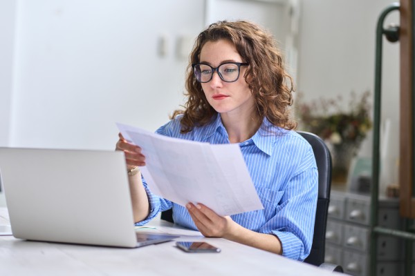 Joven mujer de negocios ocupada gerente, abogado o empleado de la empresa la celebración de documentos de contabilidad de libros de control de datos financieros o informe de marketing de trabajo en la oficina con el ordenador portátil. Gestión del papeleo