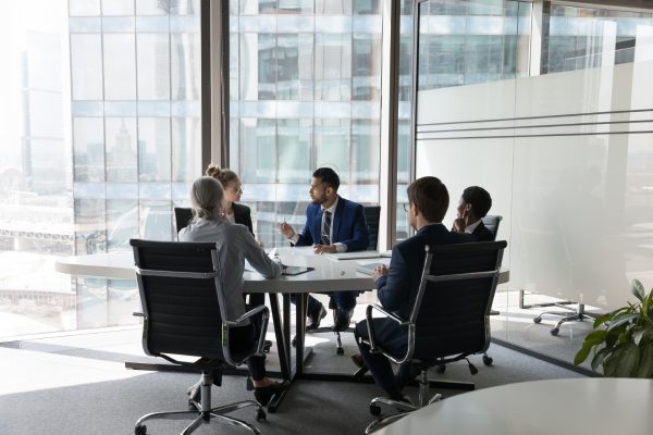 Serious team of professionals, five multi ethnic business people negotiating in modern boardroom, discuss project, consider contract terms and conditions, solve business. Formal meeting event concept