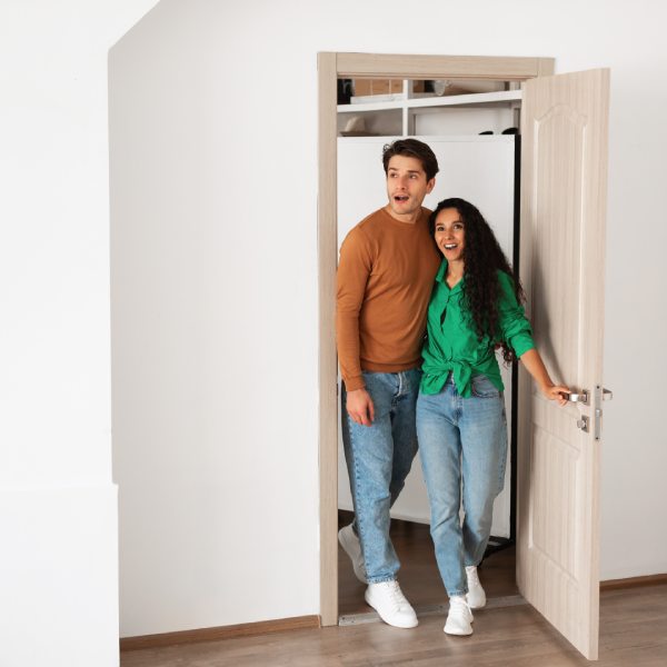 Wow. Portrait of excited emotional couple walking in their apartment, entering new home, happy young guy and lady standing in doorway of modern flat, looking at design interior together, coming inside