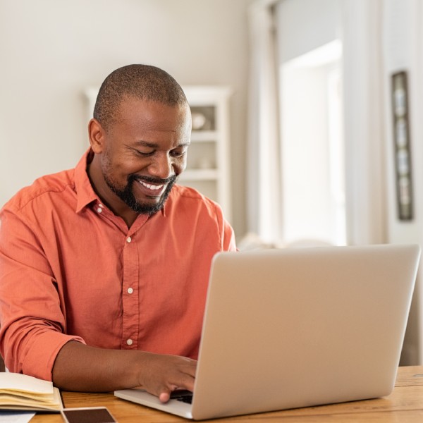 Smiling black man using laptop at home in living room.