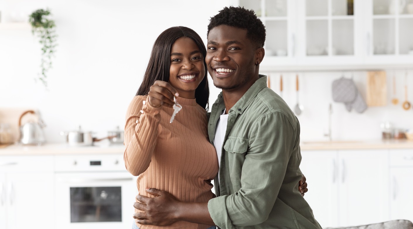 Excited african american young family showing keys to own home, happy black couple hugging, buying first house together, smiling husband and wife purchase new property.