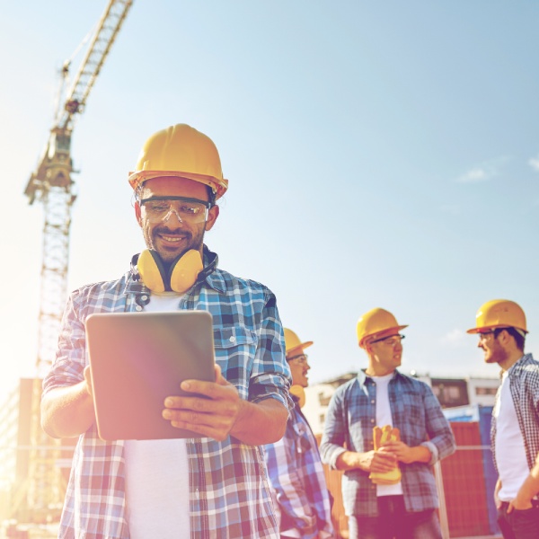 business, building, industry, technology and people concept - smiling builder in hardhat with tablet pc computer over group of builders at construction site