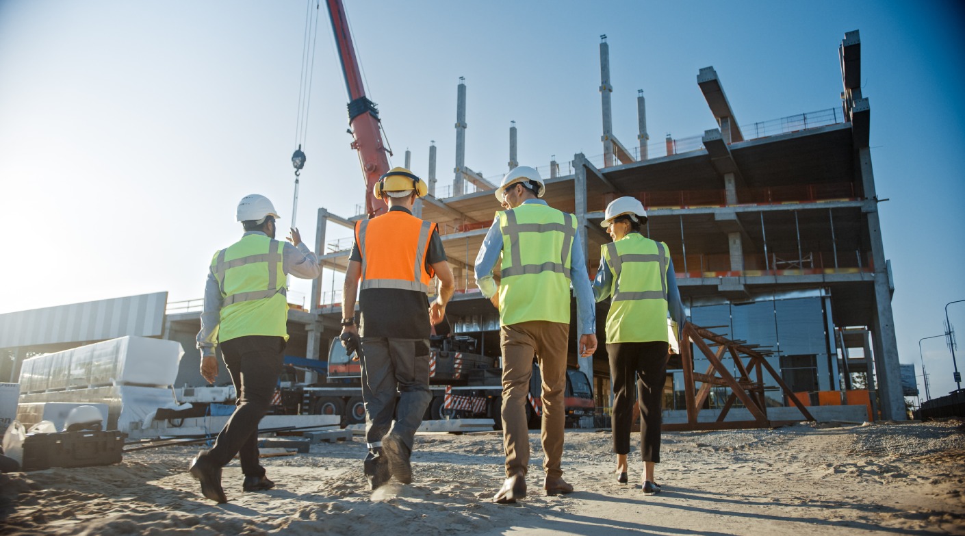 Diverse Team of Specialists Inspect Commercial, Industrial Building Construction Site. Real Estate Project with Civil Engineer, Investor and Worker. In the Background Crane, Skyscraper Formwork Frames