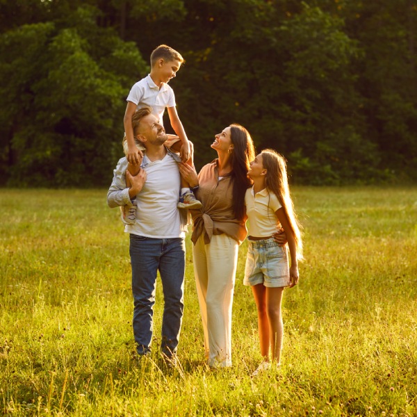 Happy family strolling in nature all together. Happy, joyful mother, father and little children walking on green grass in a beautiful park on a sunny summer evening