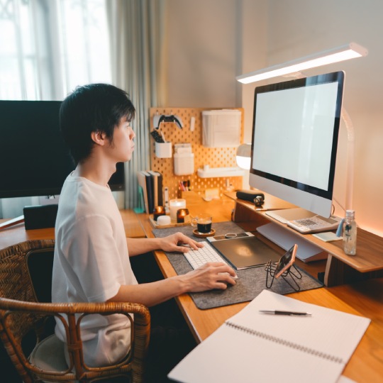 Freelance lifestyles working at home office concept. Asian man using computer productive time manage. Cozy room warming lighting ambient. Digital nomad with modern technology.