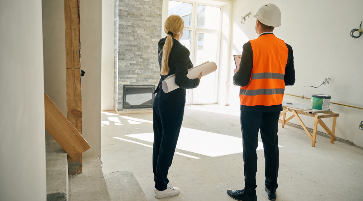 Female client and male engineer standing in room under construction