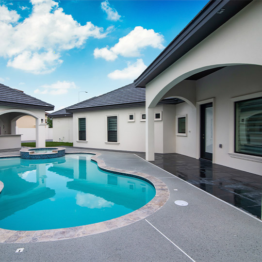 A serene pool surrounded by a patio and table, perfect for summer relaxation in a custom home setting.