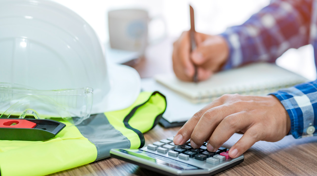 A person in a hard hat calculates costs, emphasizing the importance of professional land clearing for McAllen businesses.