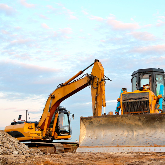 A bulldozer and backhoe sit idle on a dirt field, representing equipment used in custom home construction in McAllen, Texas.