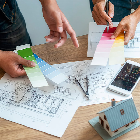 Two people collaborate on a house design, surrounded by color swatches, as part of a first-time home buyer guide.