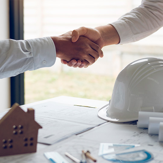 Two people shaking hands above construction plans, representing partnership in the home buying process in South Texas.