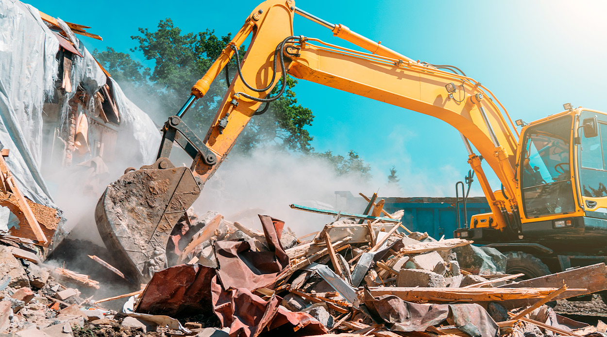 An excavator works on a rubble pile during a residential demolition, highlighting the machinery's role in construction.