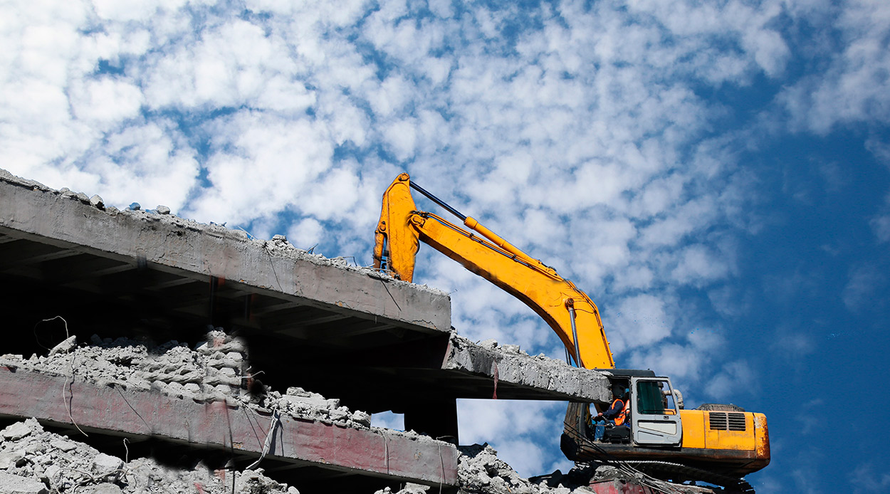An excavator is actively tearing down a building, surrounded by rubble and construction materials.