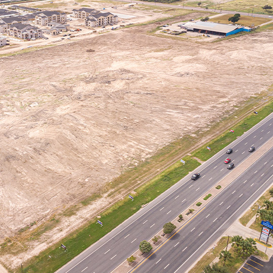 An expansive empty field adjacent to a highway, featuring a building, relevant for selecting a land clearing contractor.