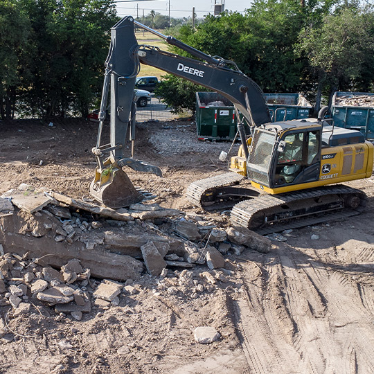 An excavator is working on a pile of rubble, clearing debris during a teardown operation.