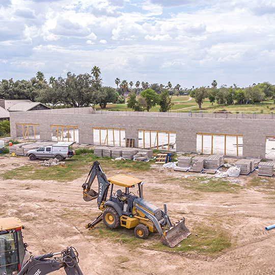 A bulldozer and tractor are actively working at a commercial construction site, surrounded by building materials.