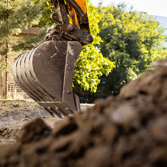 An excavator actively digging into the earth, representing the building process for custom homes in McAllen, TX.