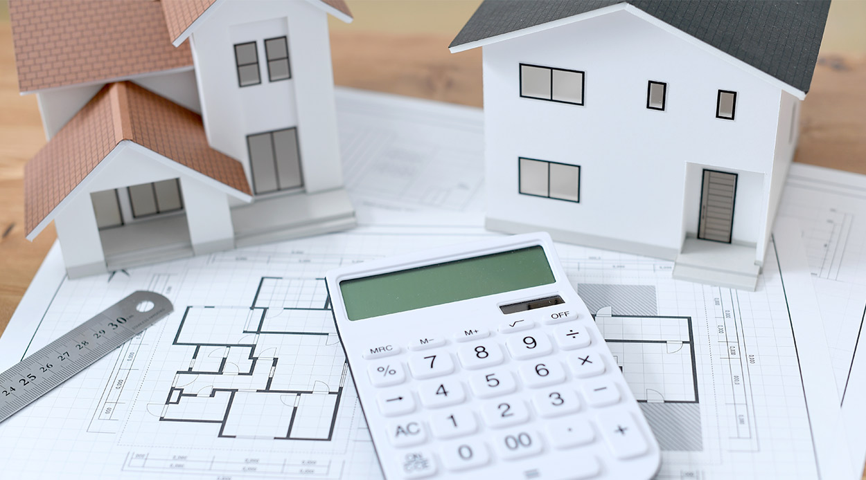 A calculator and a house model placed on a blueprint, representing the expenses of building a custom home in McAllen, TX.