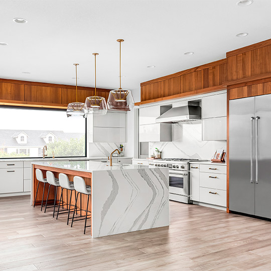 Beautiful kitchen in new luxury home with large waterfall island, stainless steel appliances, white cabinets, and hardwood floors